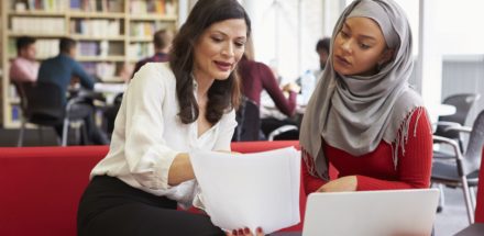 Female University Student Working In Library With Tutor