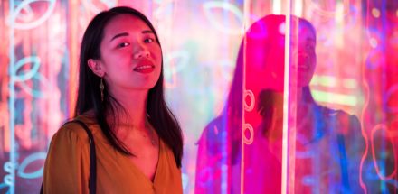 Asian woman portrait lit up by neon illuminated mirrors at night.