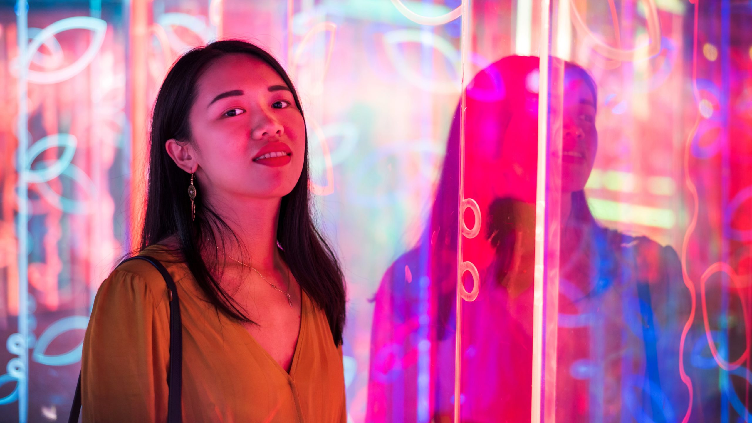 Asian woman portrait lit up by neon illuminated mirrors at night.